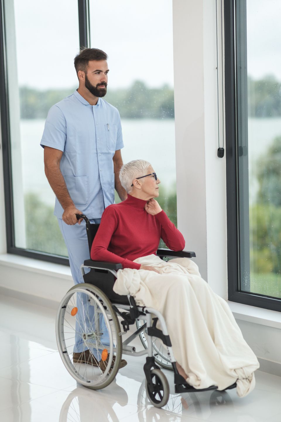 Caregiver assisting an elderly woman by a sunlit window